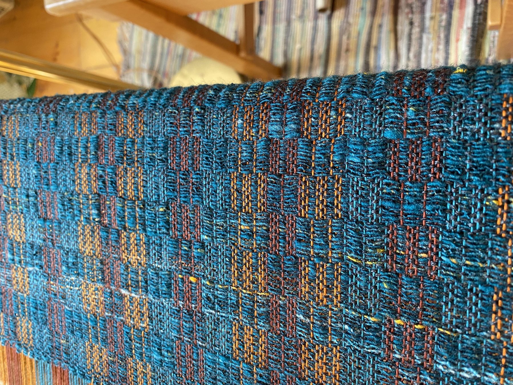 Extreme close-up of teal, rust, and gold handwoven fabric on Carol's loom